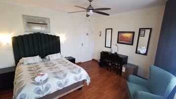 Habitación de hotel con cama, escritorio, silla, ventilador de techo y obras de arte en las paredes.