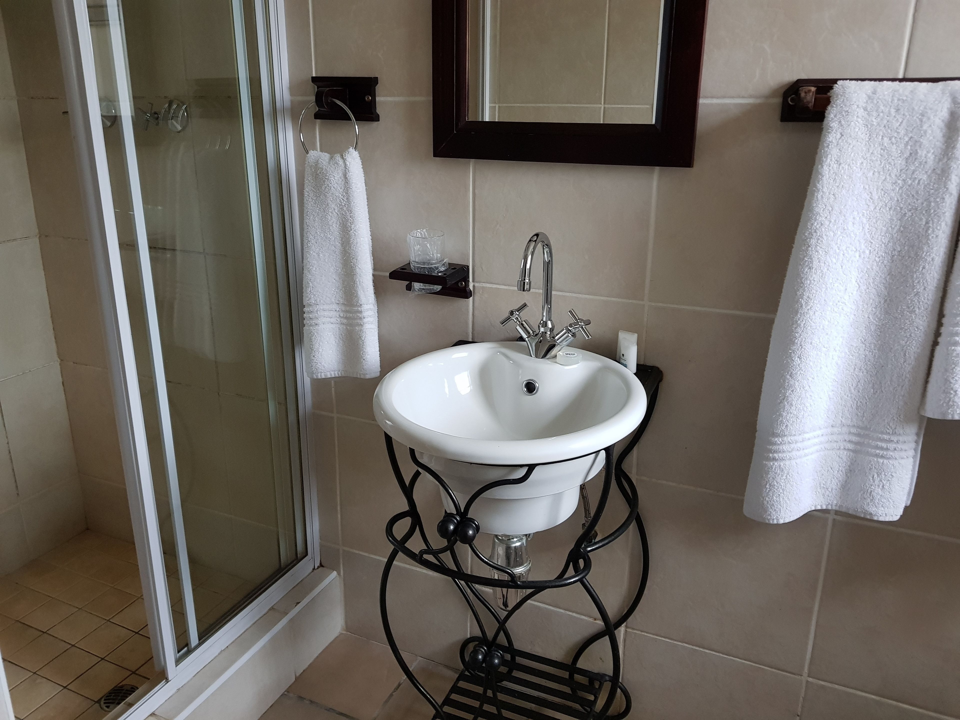 Un baño con cabina de ducha de vidrio, un lavamanos blanco sobre un pedestal negro, y dos toallas blancas colgadas en ganchos.