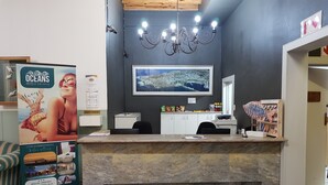 Un espace d’accueil d’hôtel avec un comptoir en marbre, un lustre, un tableau représentant une vue de la ville encadré et une boîte pour recueillir les commentaires des clients.