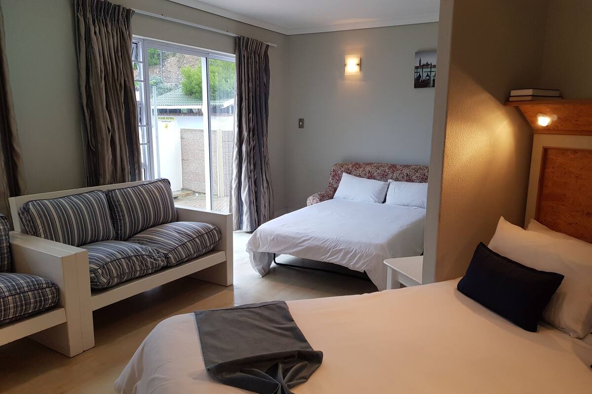 A hotel room with a bed, a sofa, a small table, and a window with curtains.