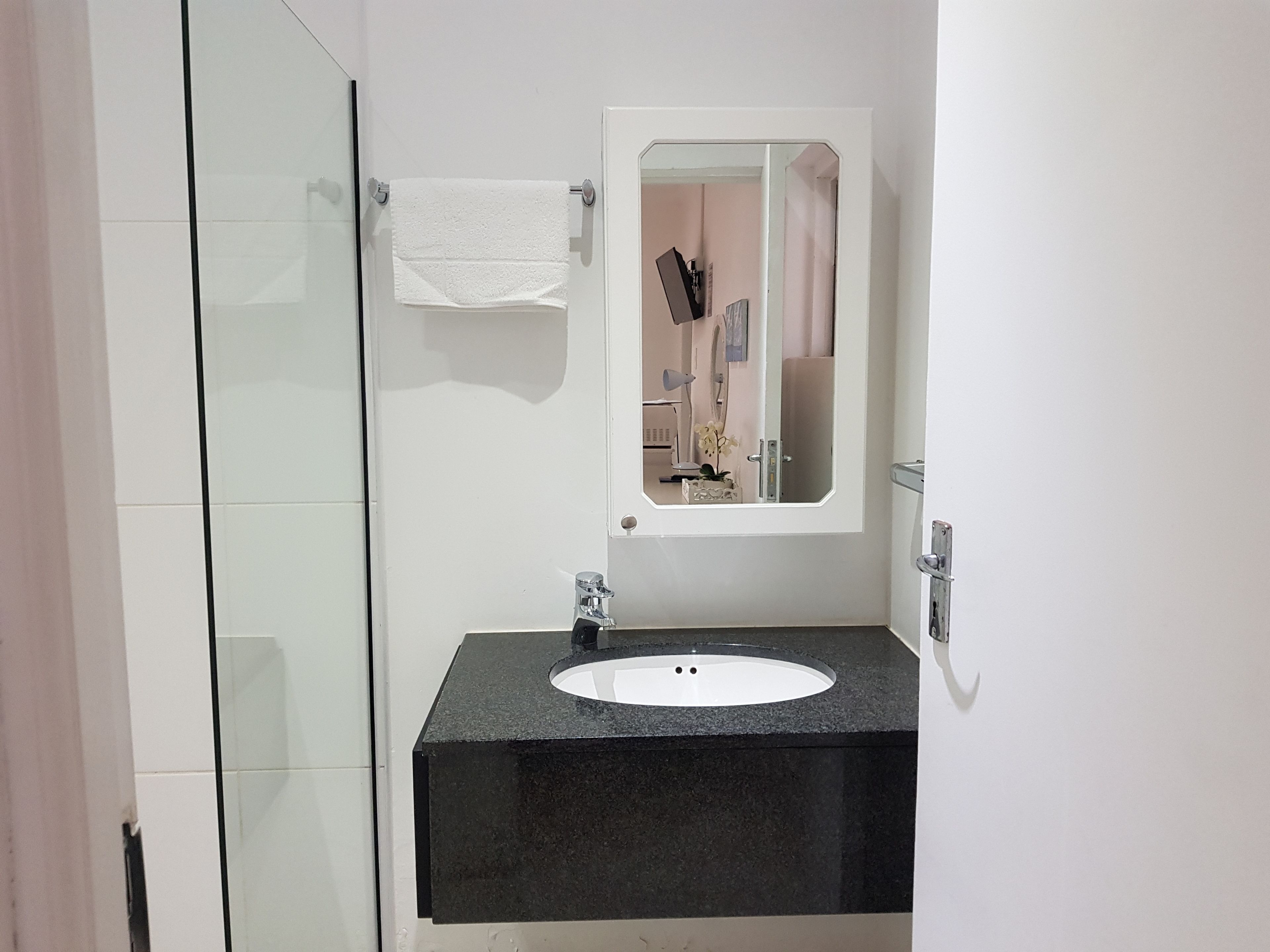 A bathroom with a glass shower enclosure, a black sink with a white countertop, and a mirror with a white frame.