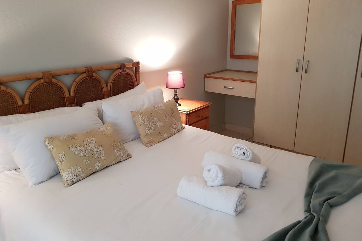 A neatly made bed with floral pillows, a bedside lamp, and a mirror above a wooden dresser.