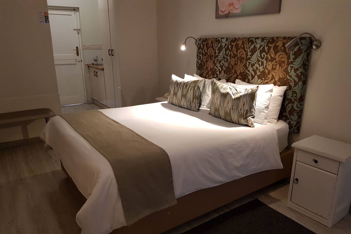 A neatly made bed with a brown headboard, a bedside table, and a small cabinet.