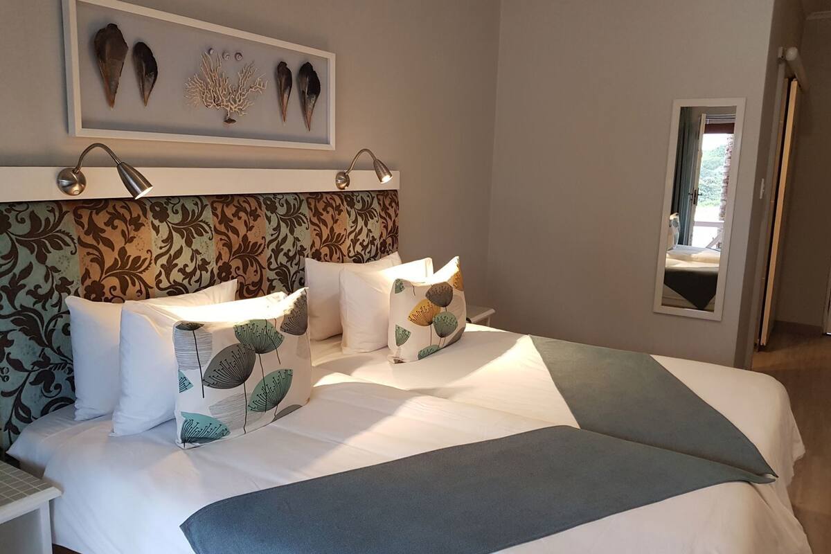 A neatly made bed with patterned pillows, a framed artwork above the bed, and a bedside table with a lamp.