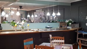 Un restaurant doté d’un bar, de chaises en bois, d’une table dressée pour le repas, de luminaires suspendus et d’un miroir qui reflète l’intérieur.