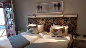 Une chambre d’hôtel avec deux lits, une tête de lit à motifs, une œuvre d’art encadrée au-dessus des lits et une table de chevet avec un téléphone et un chargeur.