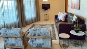 A living room with a sofa, two armchairs, a coffee table, a TV, and a chandelier. - Groenvlei Guest Farm (Stellenbosch)