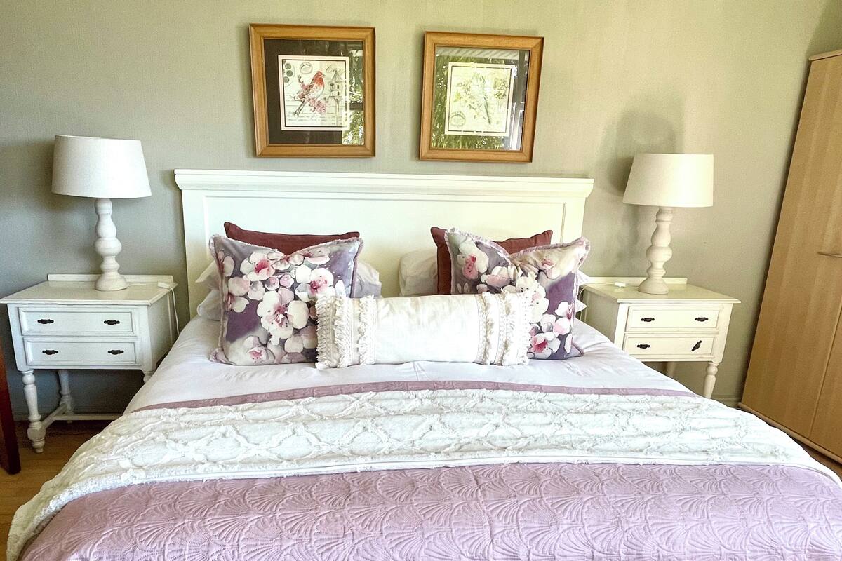 A neatly made bed with floral-patterned pillows and a white headboard. There are two bedside tables with lamps and a small drawer.