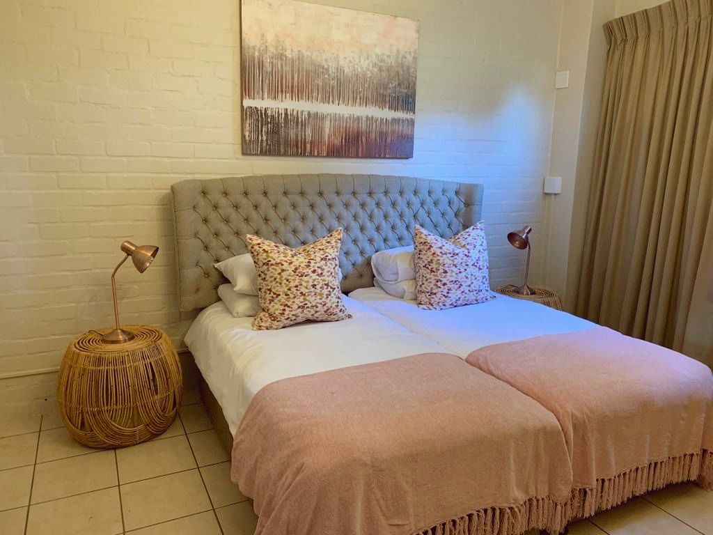 Ein Schlafzimmer mit einer gepolsterten Kopfteile, einem großen Bett mit Blumenkissen, einem gewebten Nachttisch und einer schlichten Wand mit einem einzelnen abstrakten Gemälde.