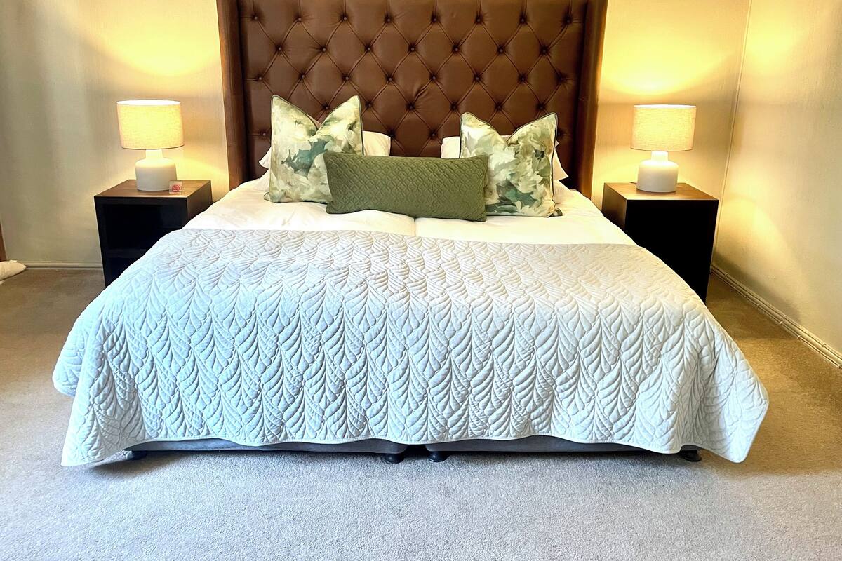 A neatly made bed with a tufted headboard, two bedside lamps, and a quilted bedspread.