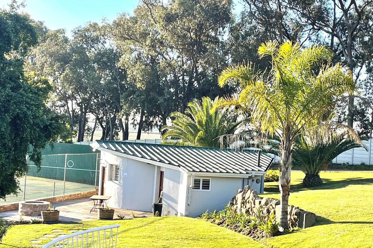 A small, single-story building with a sloped roof, surrounded by well-maintained grass lawns and various trees.
