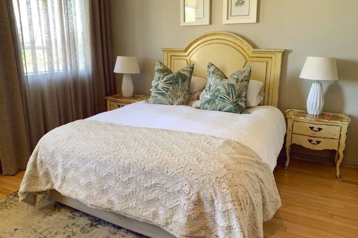 A neatly made bed with a textured white cover, two bedside tables with lamps, and a large window with curtains.