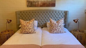 A double bed with a tufted headboard, two bedside tables with lamps, and a wall-mounted abstract painting. - Groenvlei Guest Farm (Stellenbosch)
