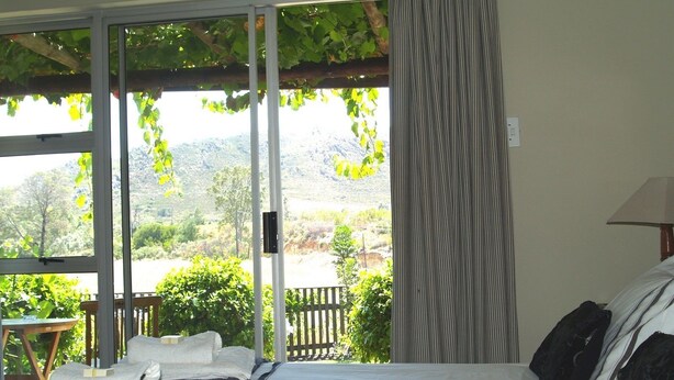 A bedroom with a bed, a view of greenery and mountains, a wooden table with towels, and a lamp. - Damas (Worcester)