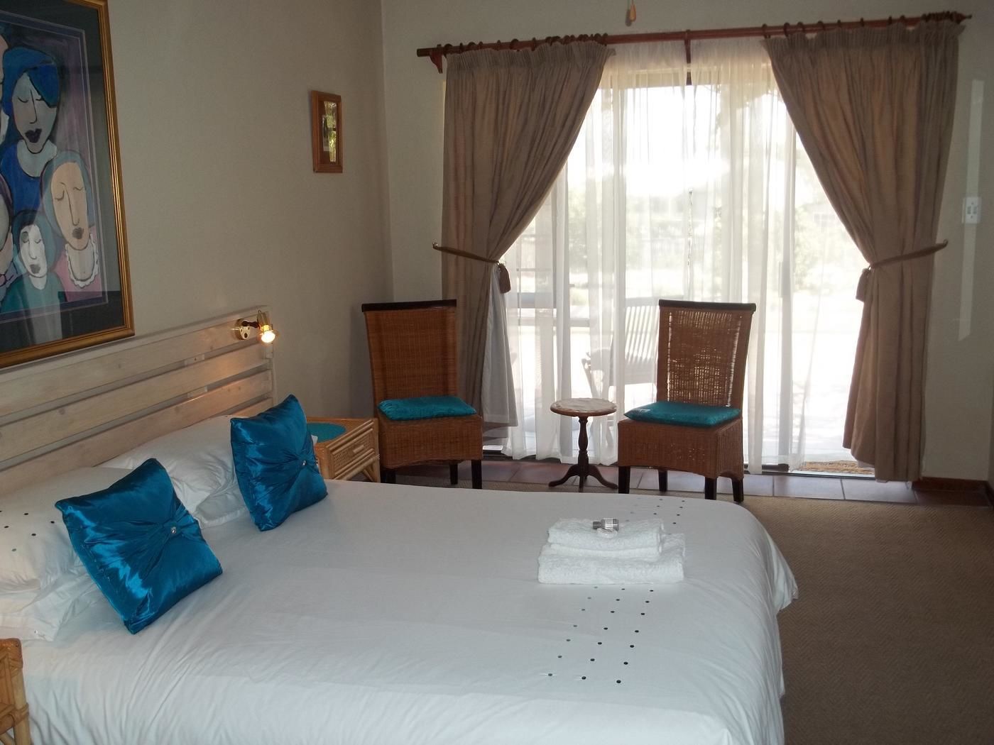 Una habitación de hotel con una cama grande, dos sillas, una mesita y un cuadro en la pared.
