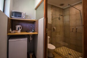 Un baño pequeño con inodoro, ducha con puerta de vidrio, lavamanos y un microondas encima, además de un pequeño espacio de almacenamiento.