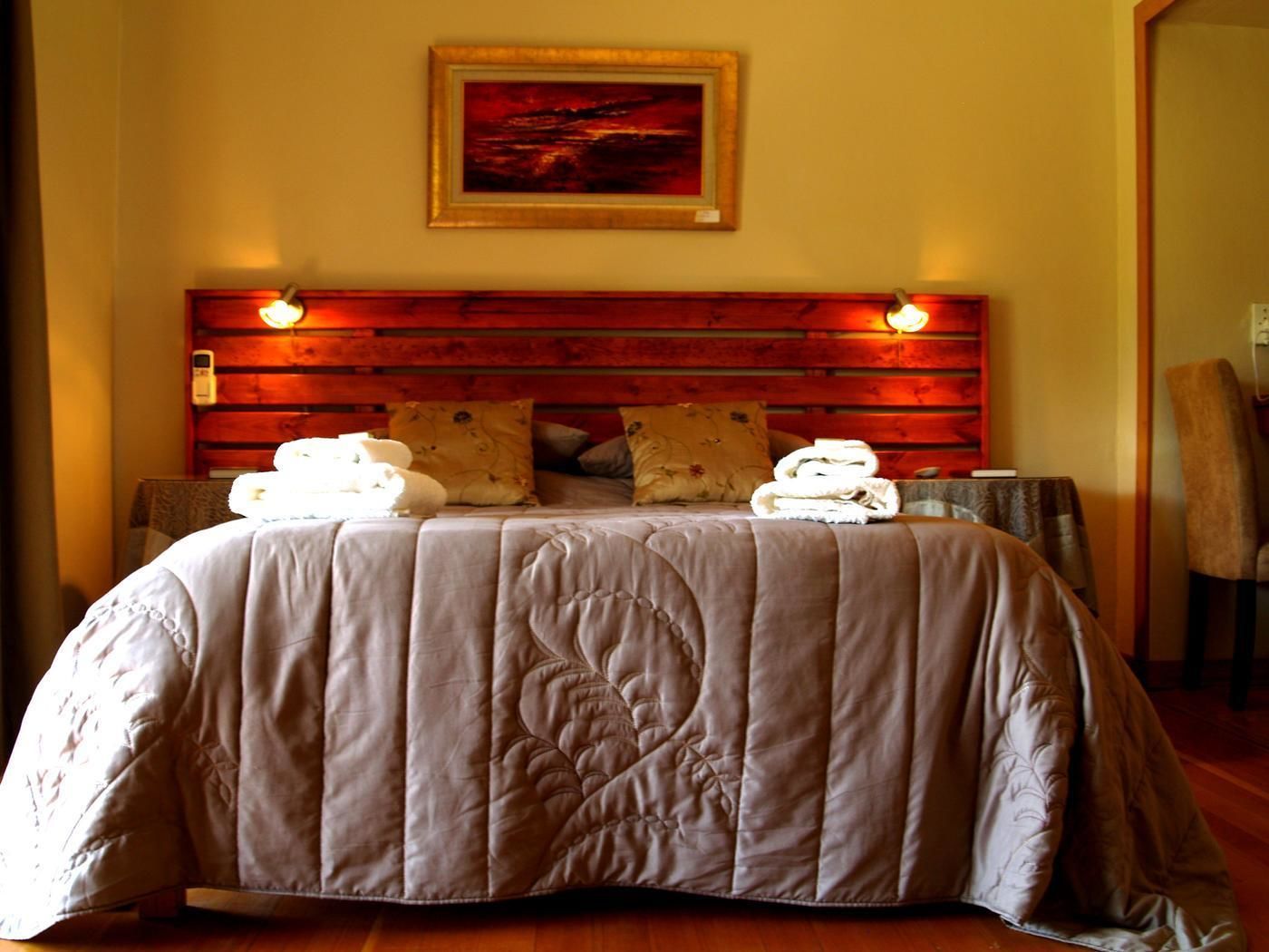 A bed with a wooden headboard, a painting above it, and two bedside lamps.