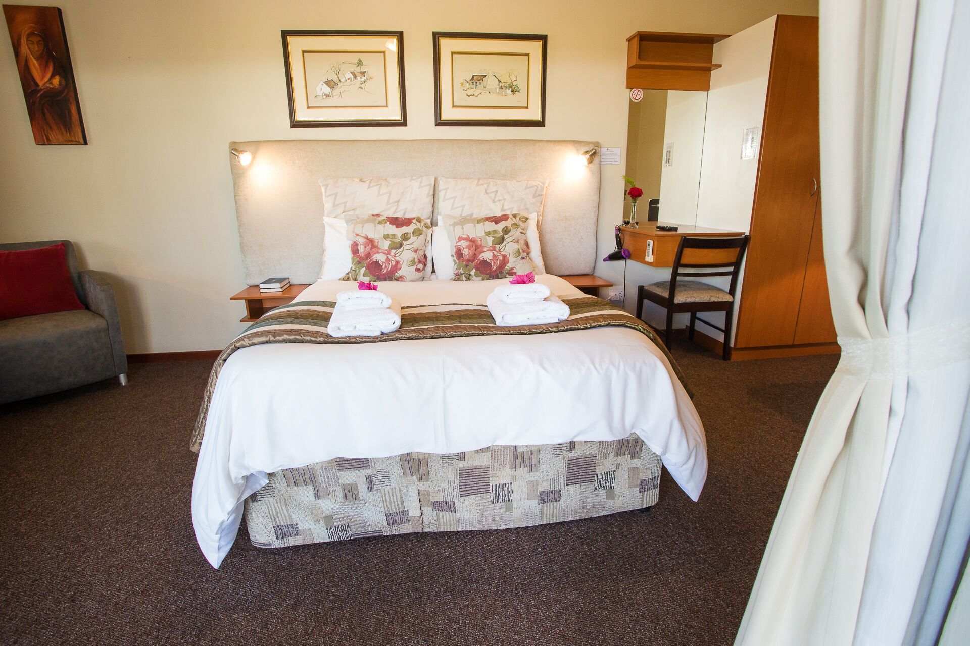 A hotel room with a large bed, a desk, a chair, a sofa, and two framed pictures on the wall.
