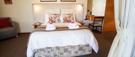 A hotel room with a large bed, a desk, a chair, a sofa, and two framed pictures on the wall.