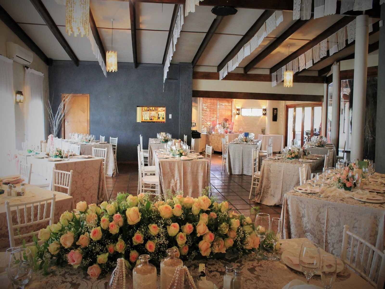 Une salle de banquet avec de nombreuses tables rondes dressées pour un événement formel, agrémentées de compositions florales et recouvertes de nappes blanches.