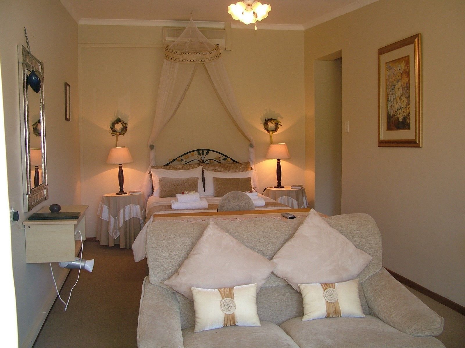 A hotel room with a bed, two bedside tables with lamps, a mirror, a sofa with decorative pillows, and a ceiling fan.
