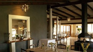 A dining area with a long table set for a meal, surrounded by chairs. There are hanging lights, a large mirror, and a fireplace in the background. - Damas (Worcester)