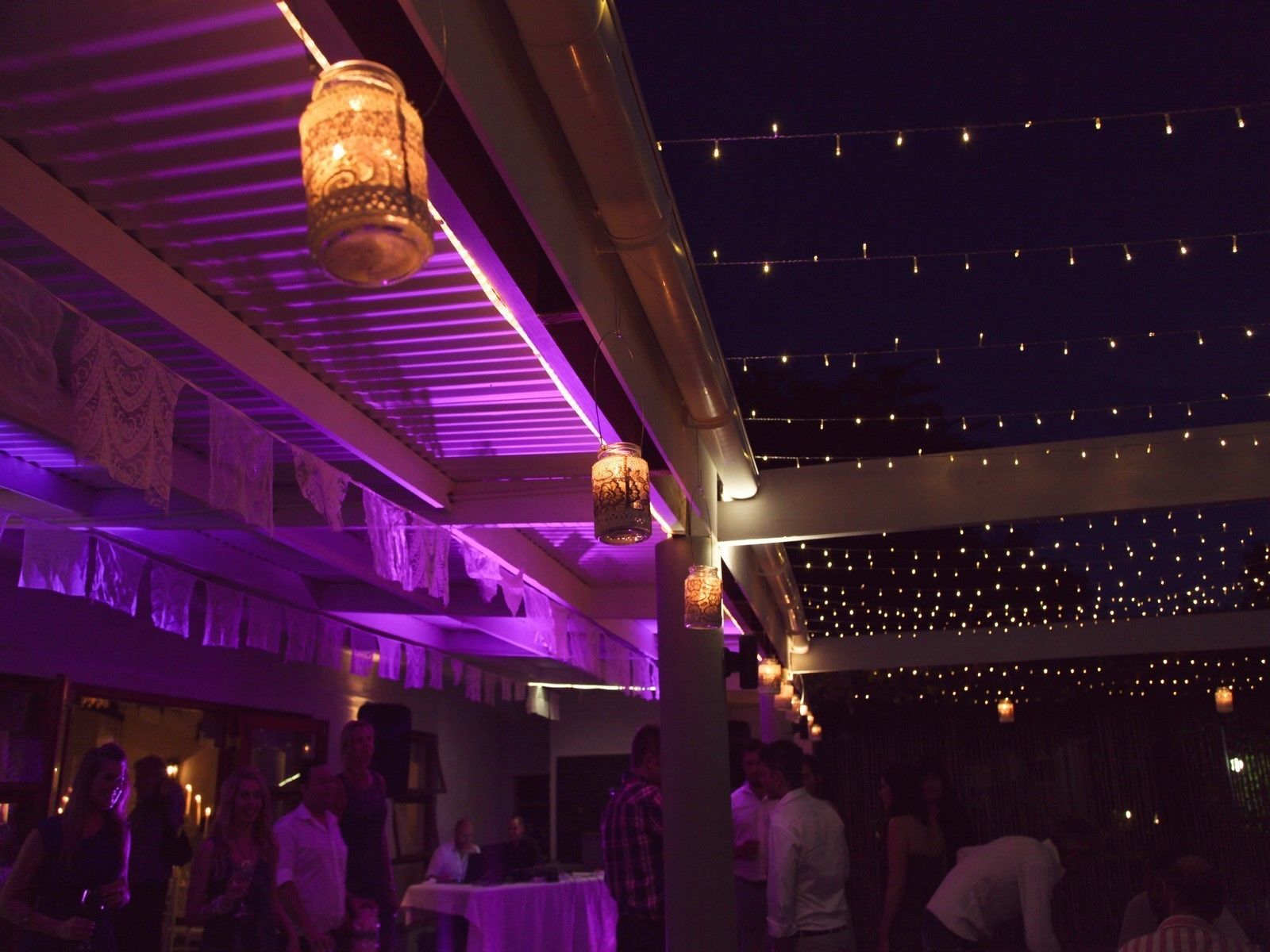 An indoor venue with tables and chairs, string lights, and hanging lanterns.