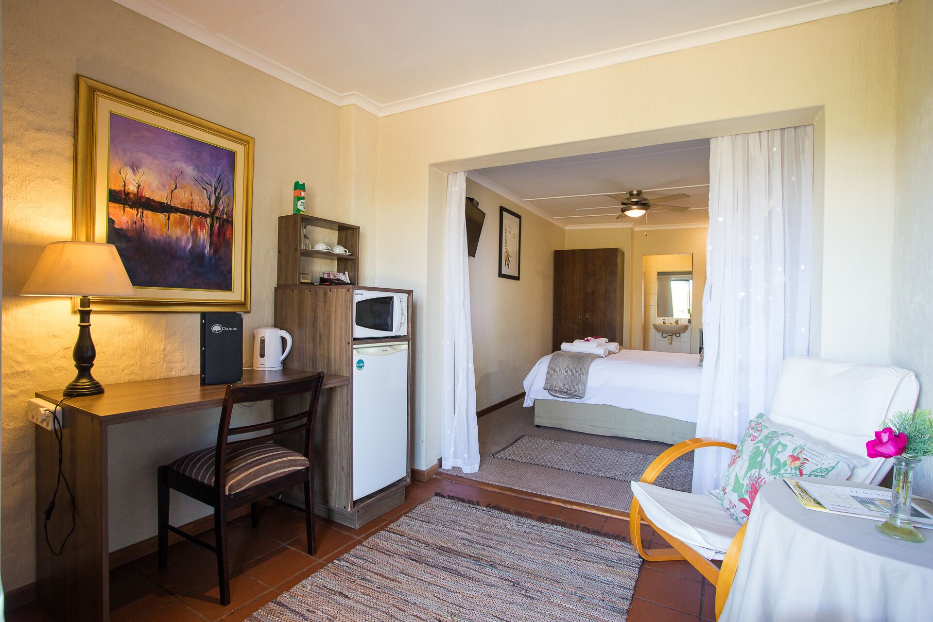 Habitación de hotel con escritorio, silla, cama y una pequeña mesa con un florero.