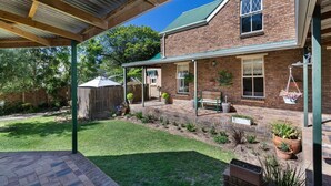 Een bakstenen huis met een overdekte patio, een omheinde achtertuin en een hangende bloempot.