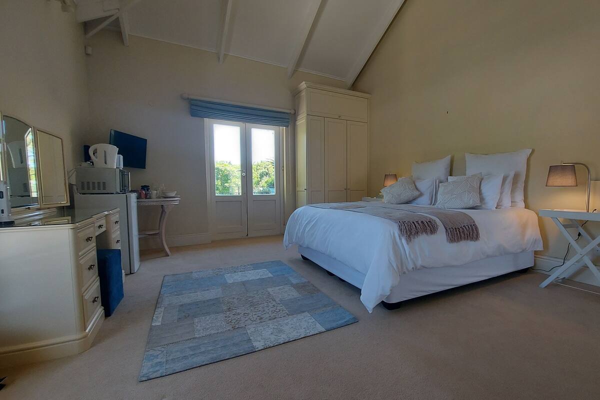 A bedroom with a bed, bedside table, lamp, desk, and a window.