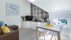 Een moderne keuken met witte kastjes, een magnetron en een koffieapparaat. Er is een eethoek met een witte tafel en stoelen.