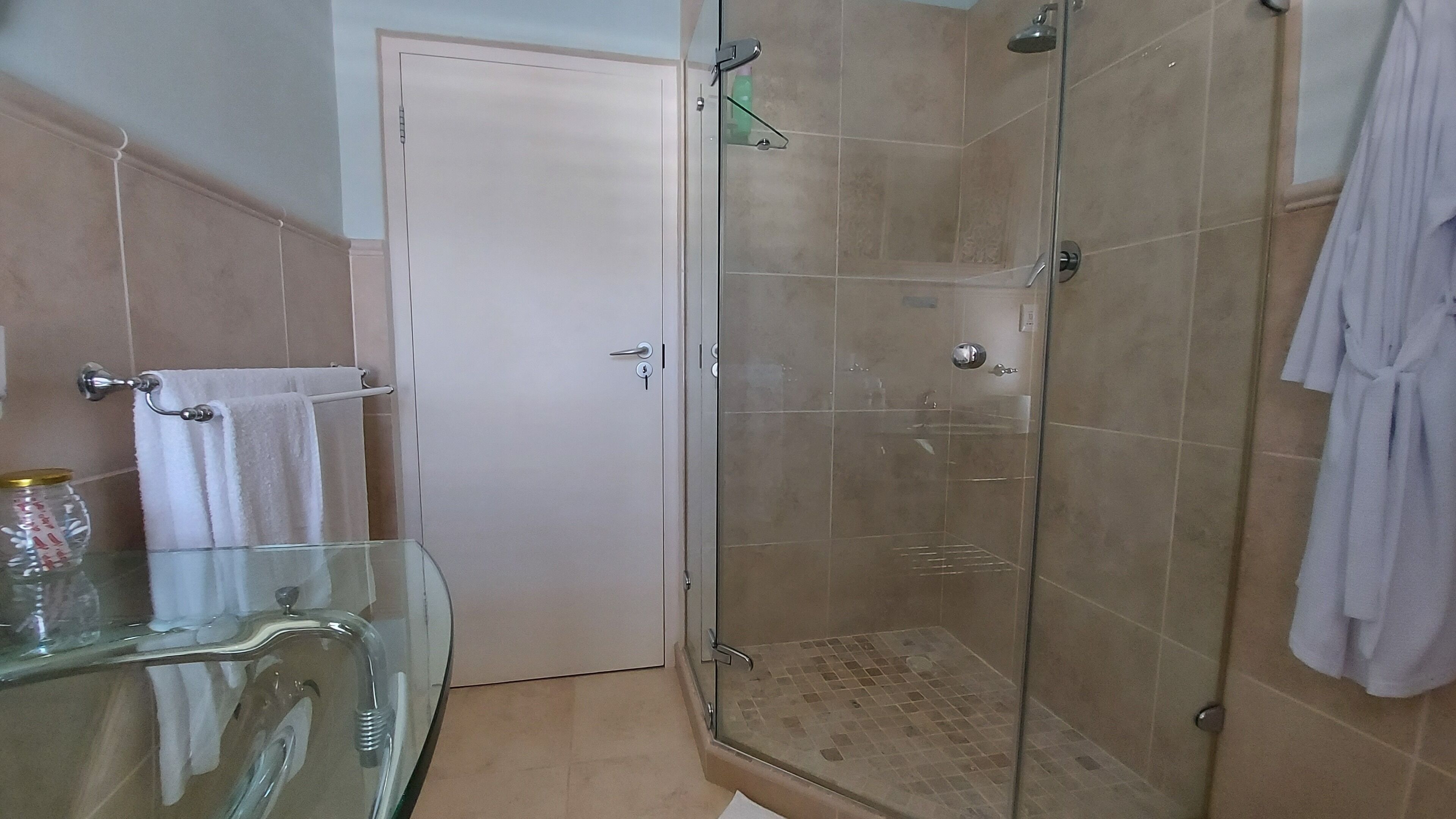 Un baño con cabina de ducha de vidrio, lavamanos de vidrio y una puerta blanca.