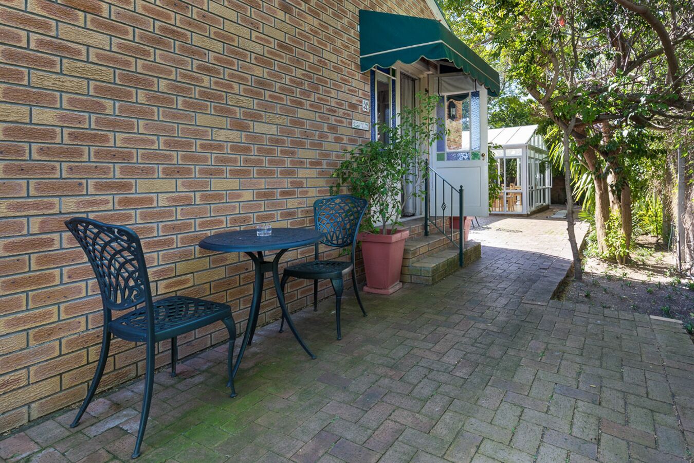 A brick building with a green awning, a small patio with two metal chairs and a table, and a potted plant.