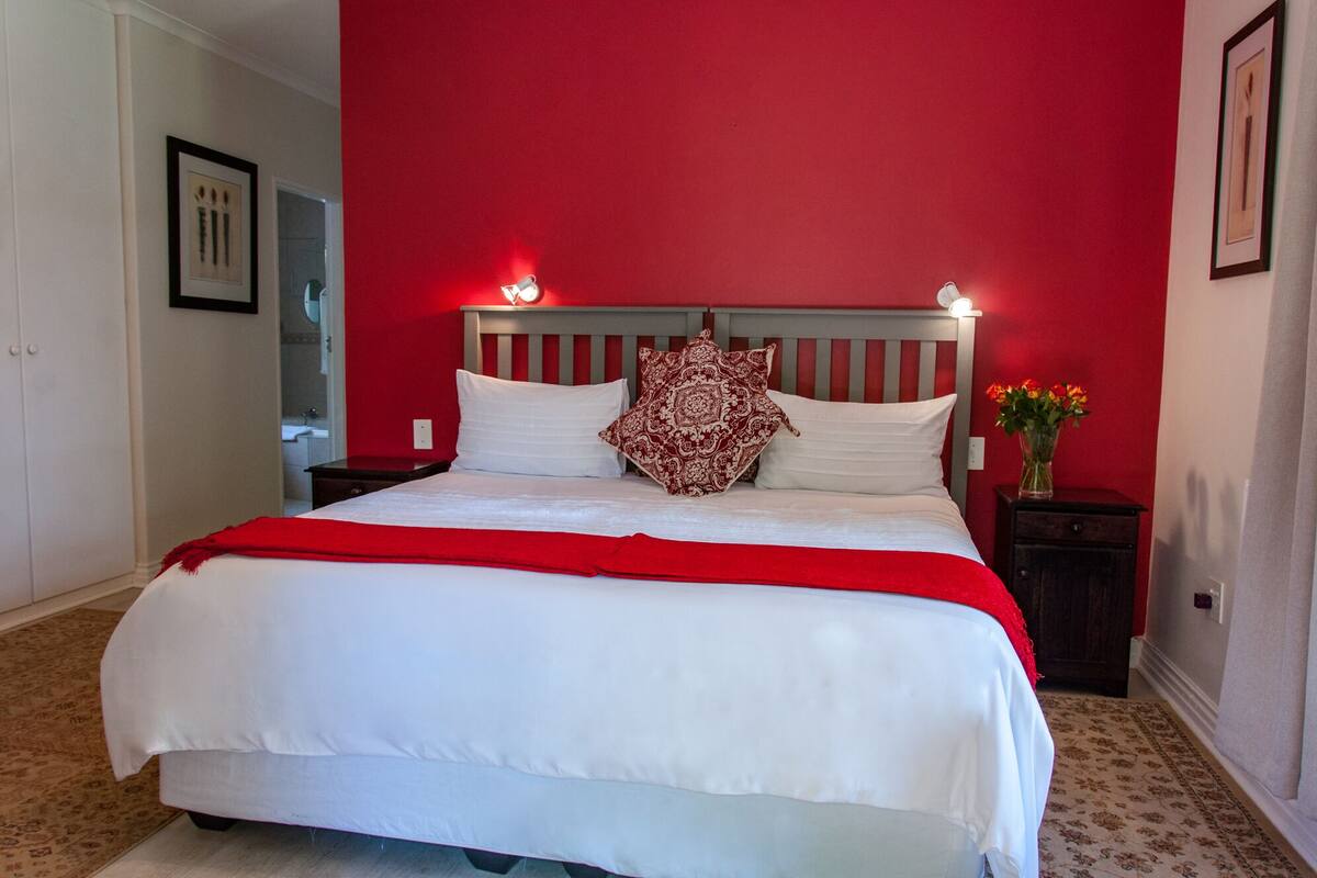 A bed with white bedding and a red throw, a nightstand with a vase of flowers, and a red wall.