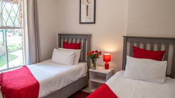 Une chambre d’hôtel avec deux lits, chacun agrémenté de draps blancs et d’oreillers rouges, une petite table de chevet avec une lampe rouge et un tableau encadré au mur.