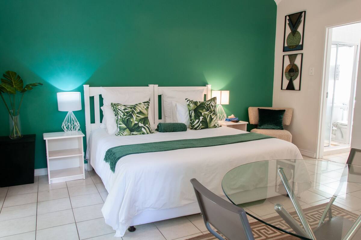 A modern bedroom with a large bed, a glass table, and a green wall.