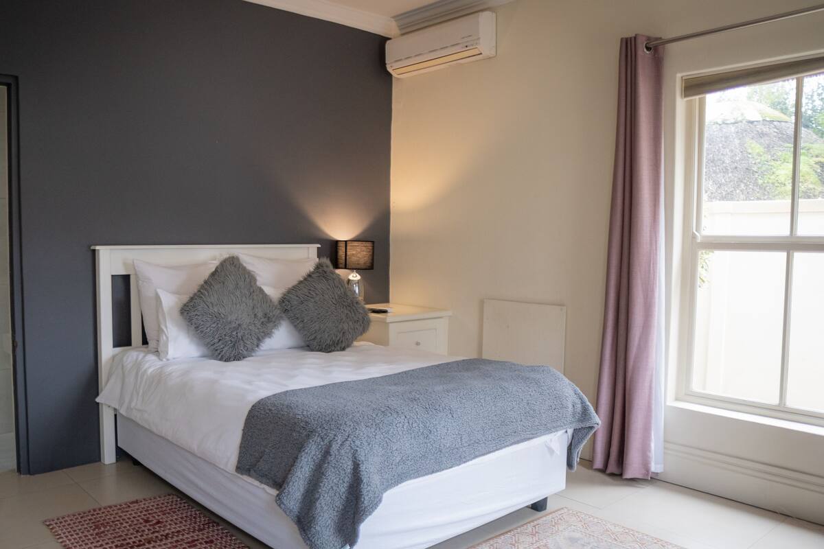 A bedroom with a bed, bedside table, lamp, and a window with curtains.