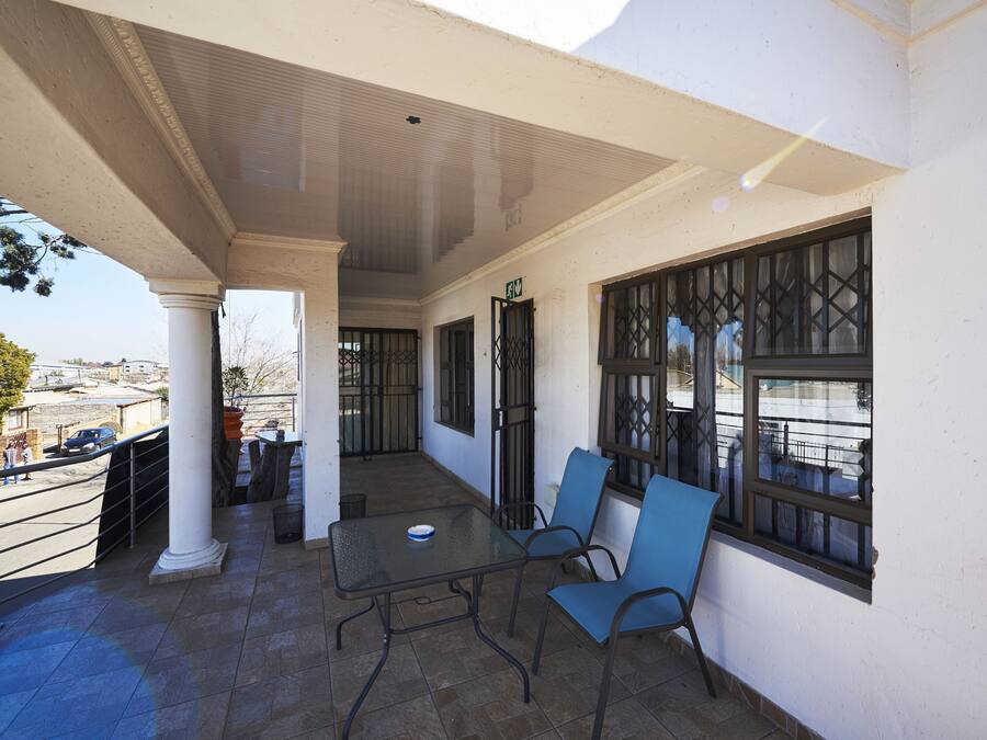 Un patio al aire libre con mesa y sillas, un área cubierta con columnas y vistas a la ciudad.