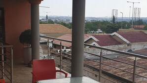 A balcony with a table and chairs, overlooking a residential area with red-roofed houses. - Flossie’s Bed and Breakfast (Soweto)