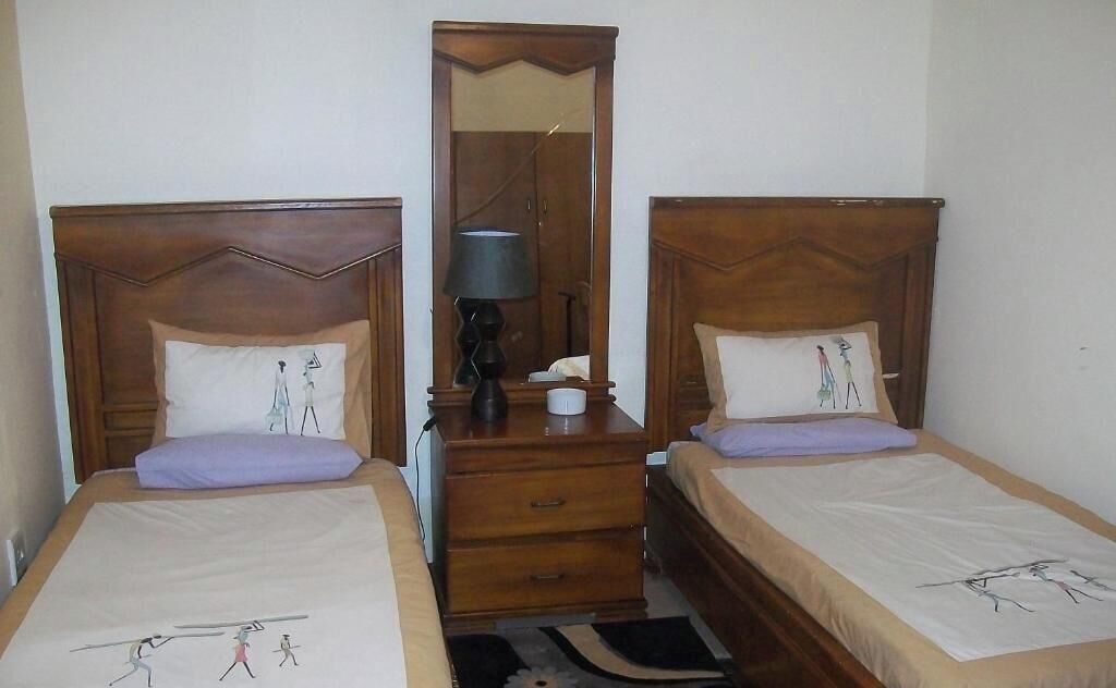 Dos camas individuales con cabeceros de madera, una mesita de noche con lámpara y un espejo entre ellas.