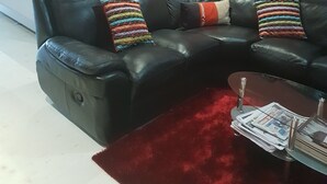 A living room with a black leather sofa, a red rug, and a coffee table with newspapers. - Flossie’s Bed and Breakfast (Soweto)