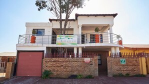 A two-story building with a balcony, a red garage door, and a brick wall. - Flossie’s Bed and Breakfast (Soweto)
