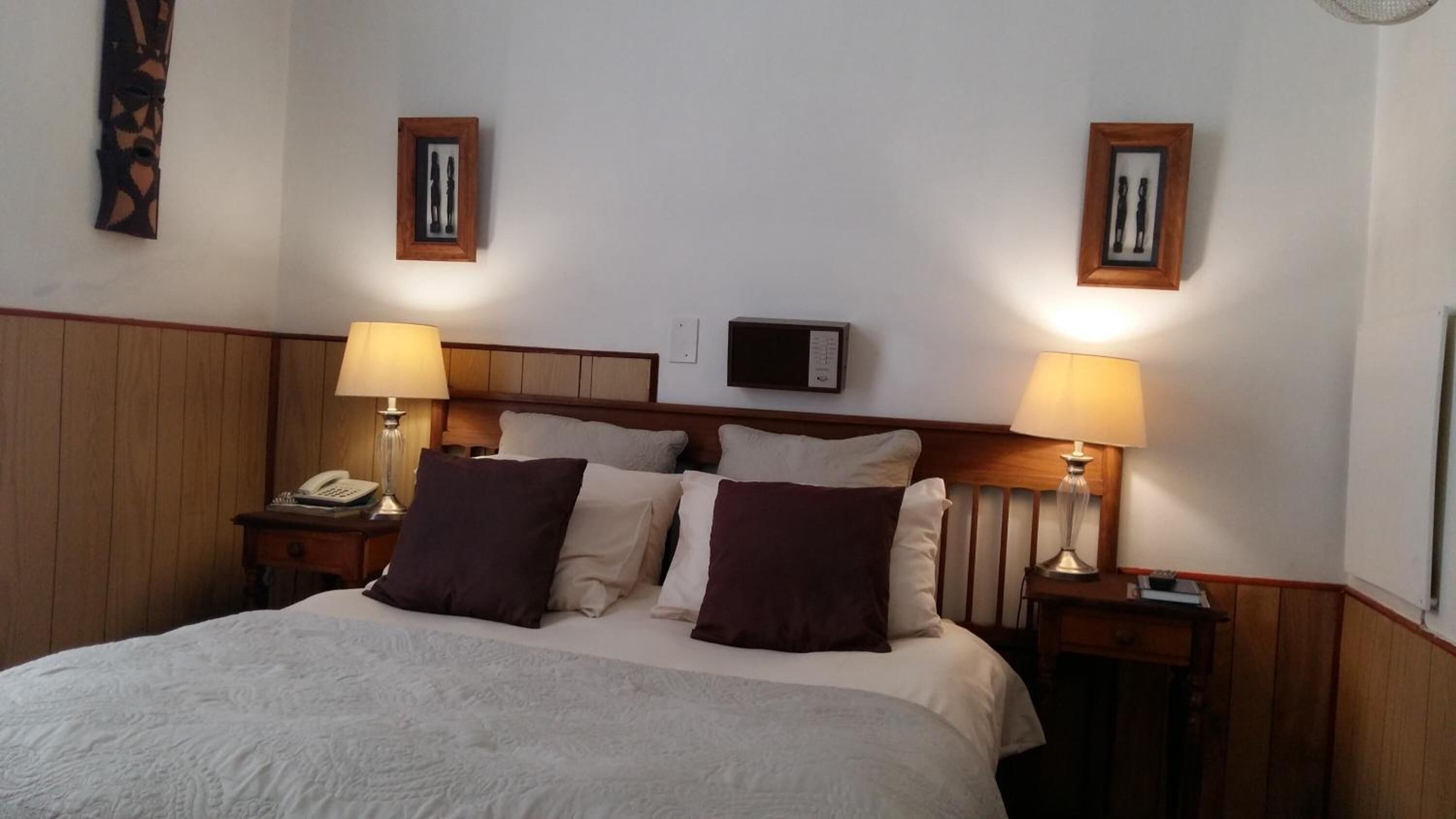 A hotel room with a large bed, two bedside tables with lamps, a wooden headboard, and two framed pictures on the wall.