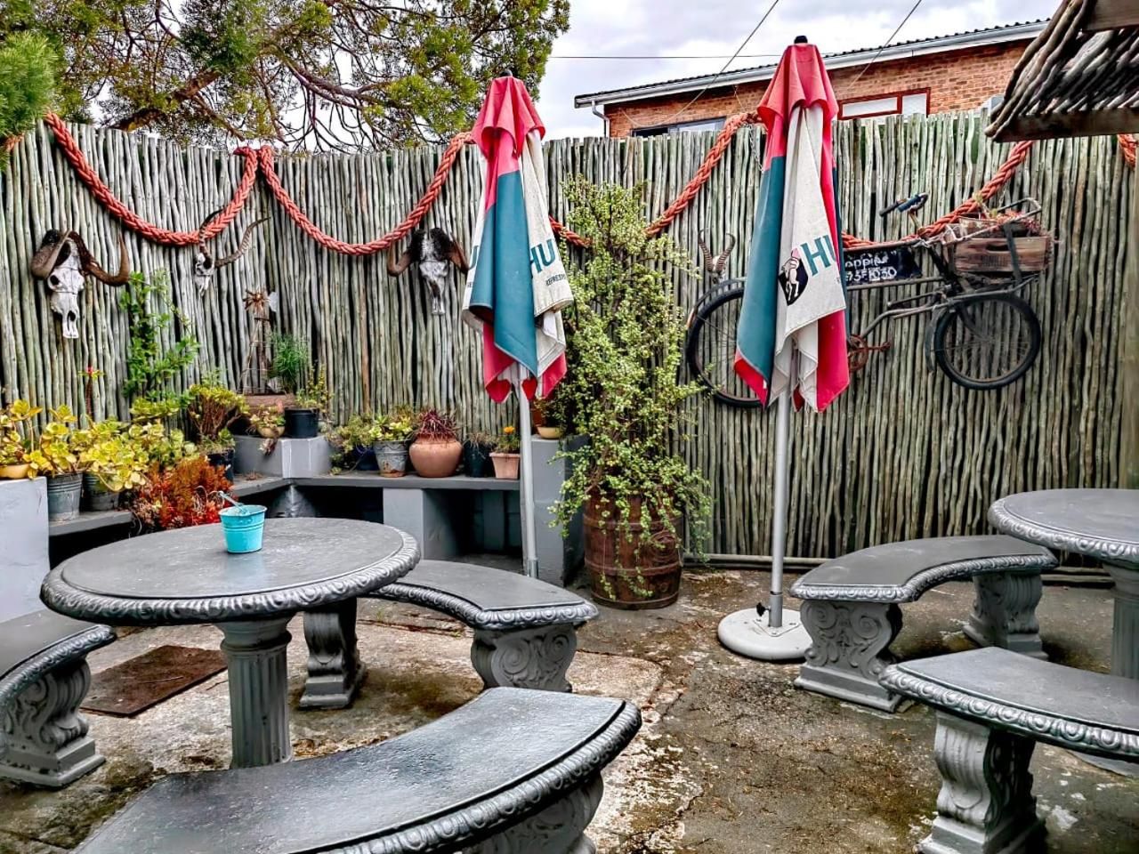 Un patio con mesas y bancos de piedra, una cerca de madera y plantas en macetas.