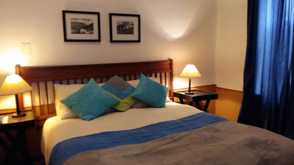 Habitación de hotel con cama, dos lámparas de noche y dos cuadros en la pared.