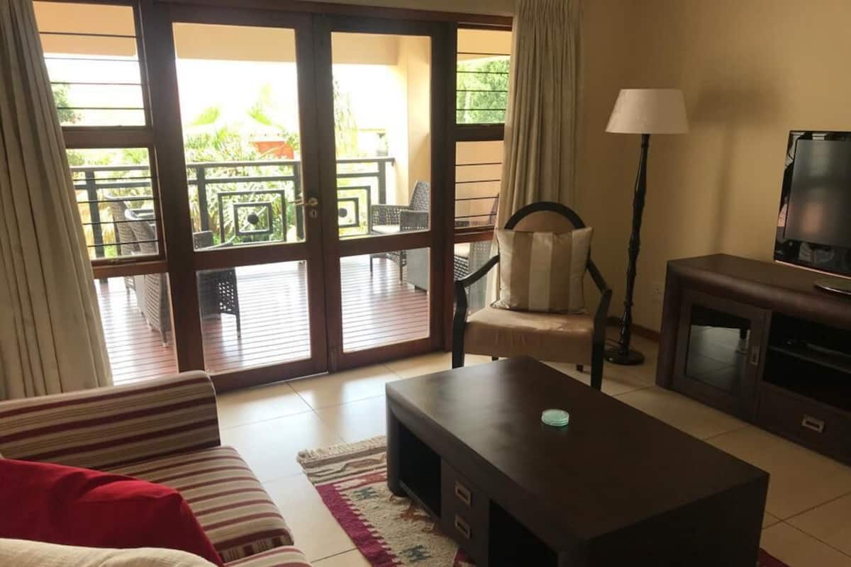 Ein Wohnzimmer mit einer Couch, einem Couchtisch, einem Fernseher und einem Balkon mit Gartenmöbeln.
