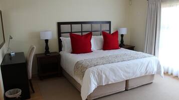 A neatly arranged hotel room with a large bed, two bedside tables with lamps, a desk, and a chair.