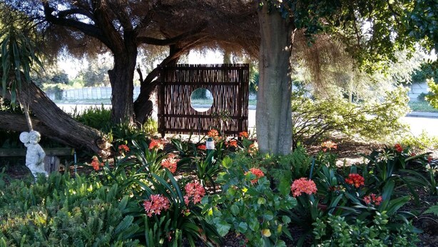 Un jardin avec une clôture en bois, une statue et diverses plantes à fleurs.