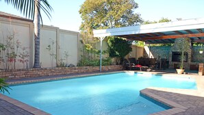 Une piscine avec un patio couvert, un mur en briques et une cheminée en briques.