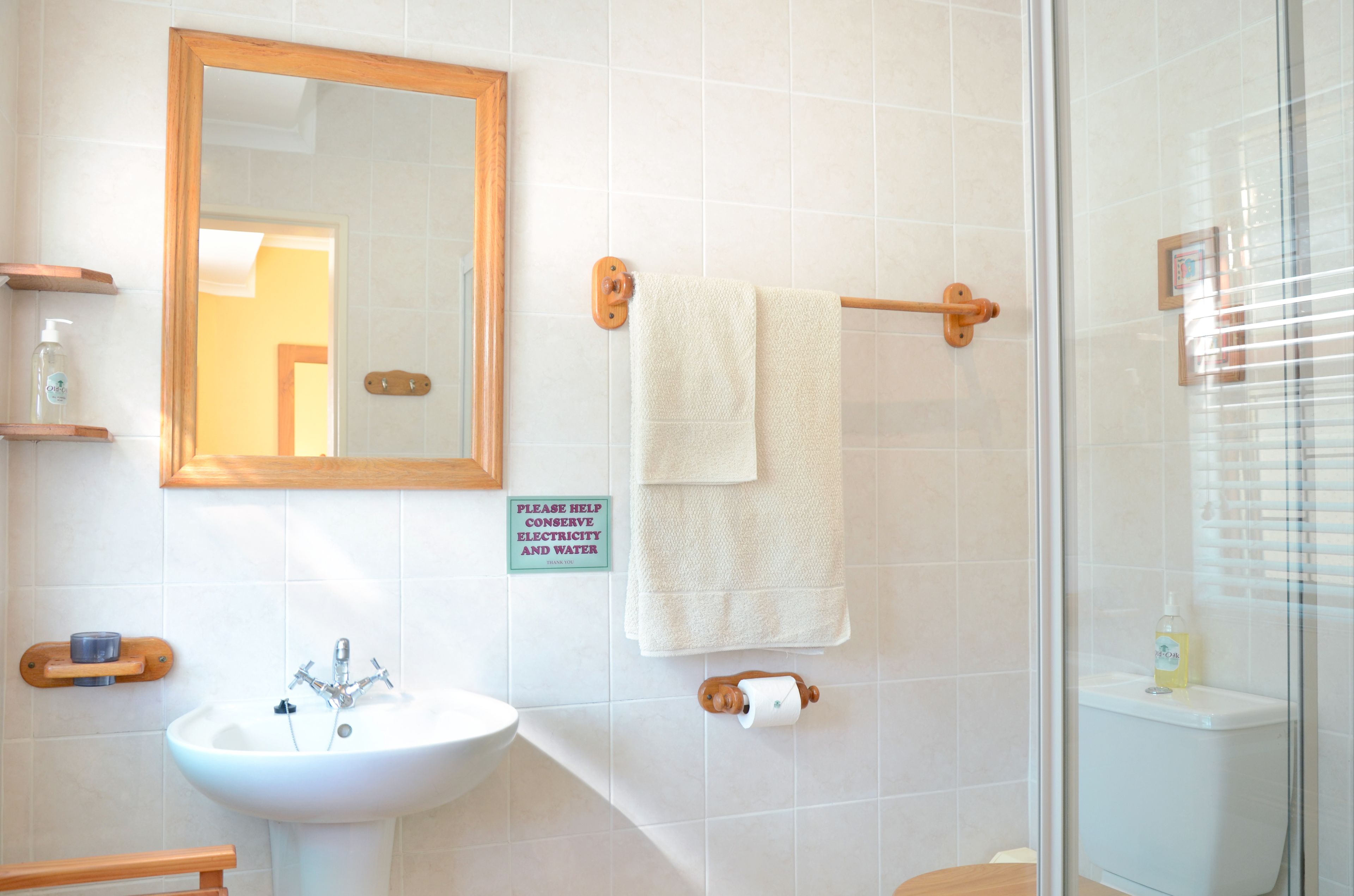 A bathroom with a sink, mirror, towel rack, and a sign encouraging to conserve electricity and water.